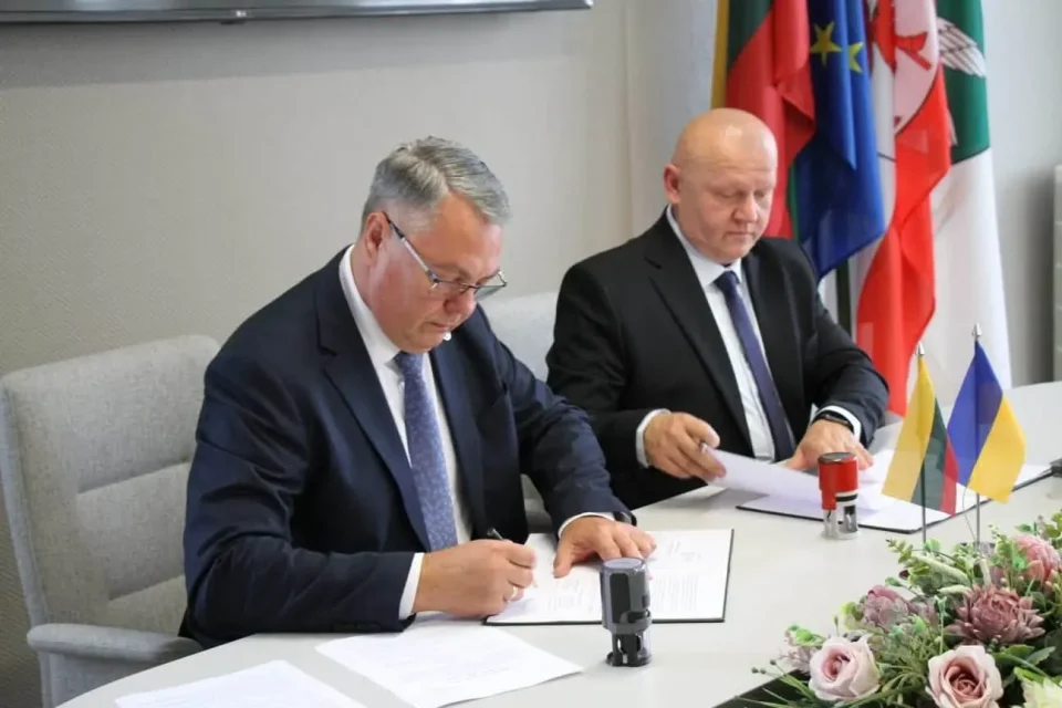 Двоє чоловіків у костюмах підписують угоду за столом із прапорами Литви та України